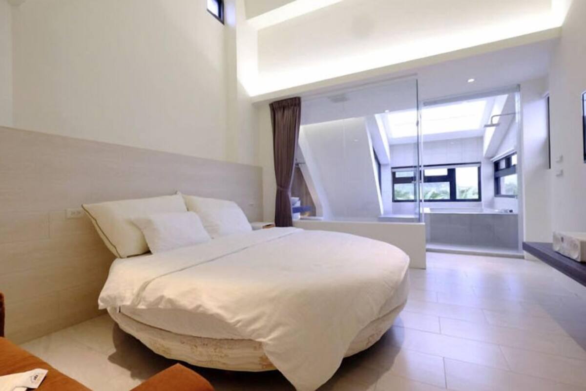 A modern bedroom with a large bed, a wooden headboard, and a glass door leading to a balcony.