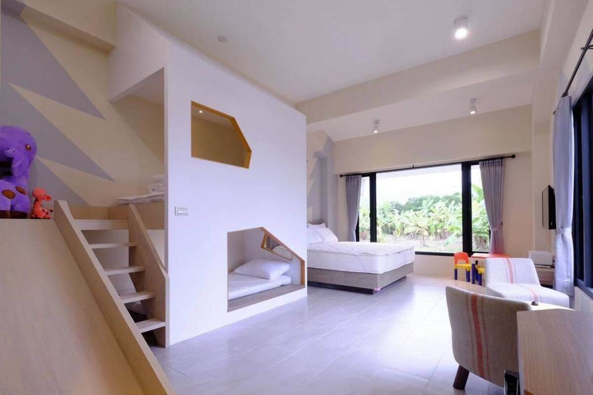 A modern hotel room with a staircase, a bed, a sofa, and a large window offering a view of greenery.