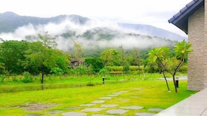 A garden with a stone pathway, lush greenery, and a building with a stone facade. - Take Sunny B&B (Shoufeng)