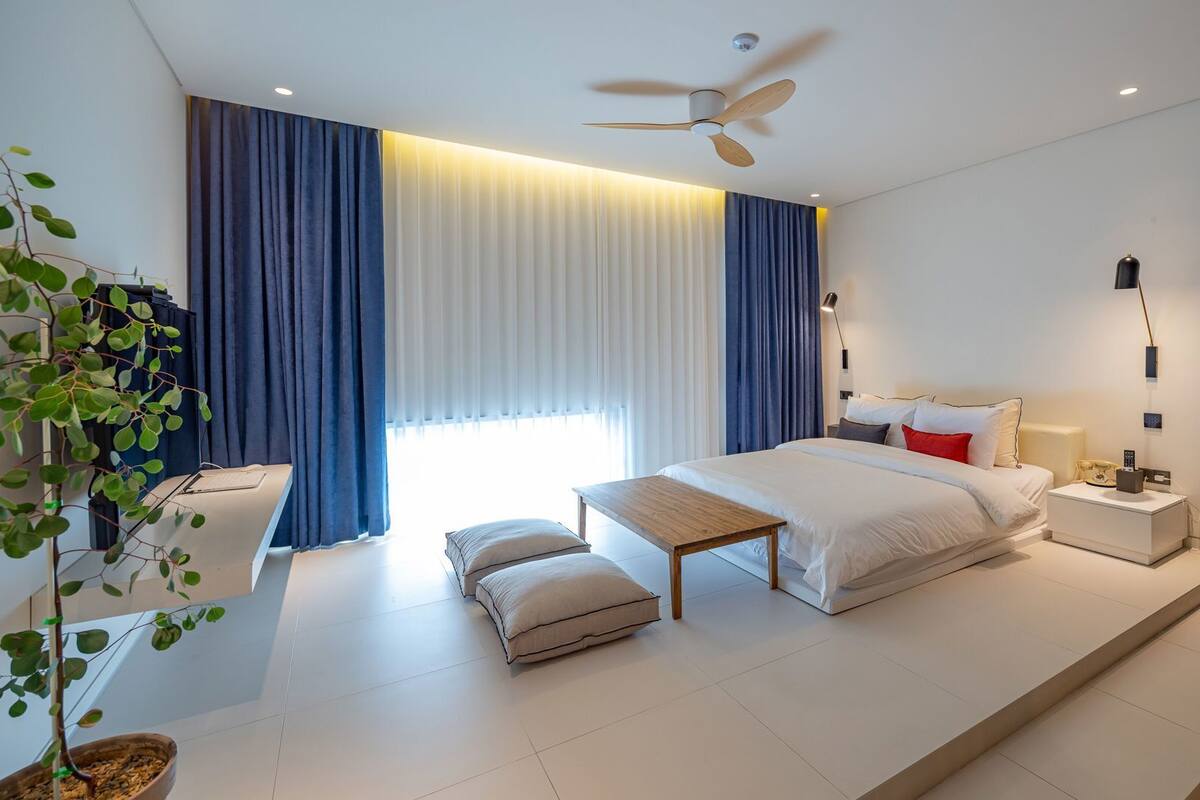 A modern hotel room with a large bed, bedside tables, a ceiling fan, and a potted plant.