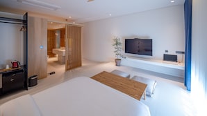 A modern hotel room with a large bed, a TV, a desk with a computer, a plant, and a bathroom visible through a sliding door. - Jeonju Hotel Barahan (Jeonju)