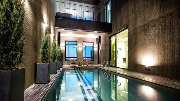 An indoor swimming pool with a modern design, featuring a clear pool, wooden deck, and seating area with chairs. - Jeonju Hotel Barahan (Jeonju)