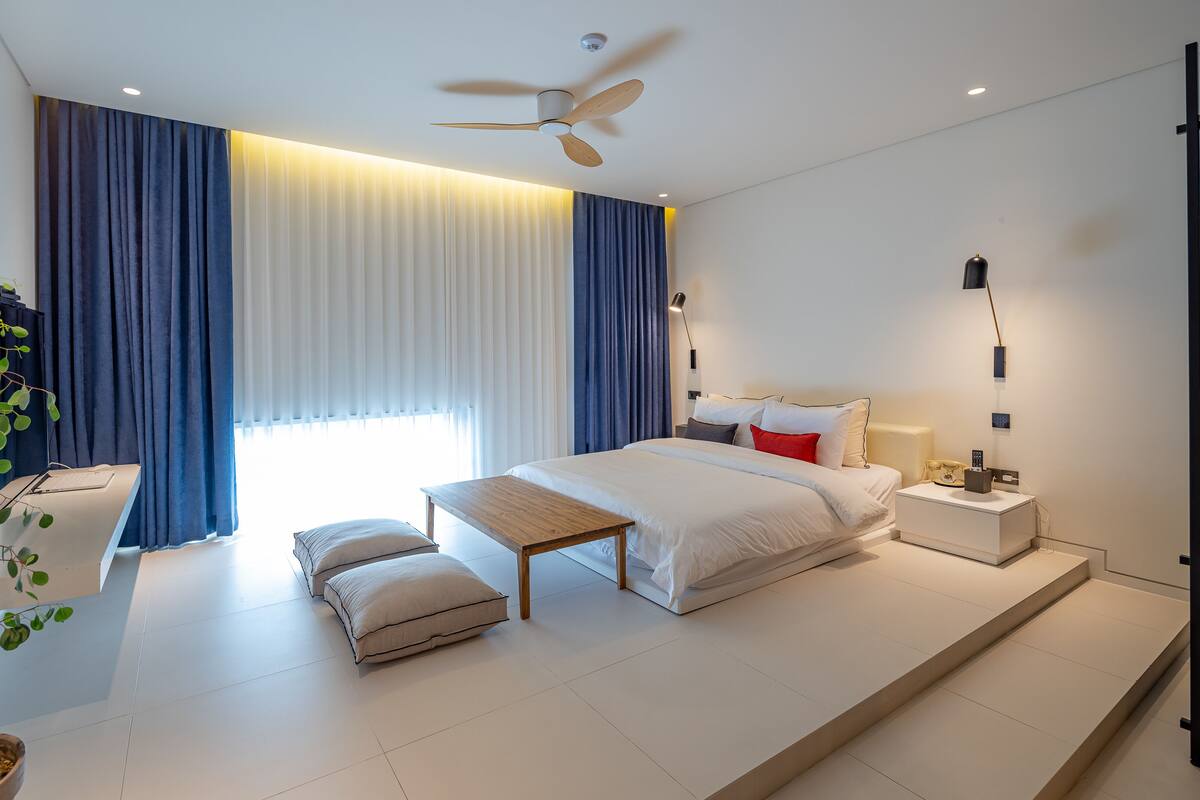 A modern bedroom with a large bed, bedside tables, a ceiling fan, and a potted plant.