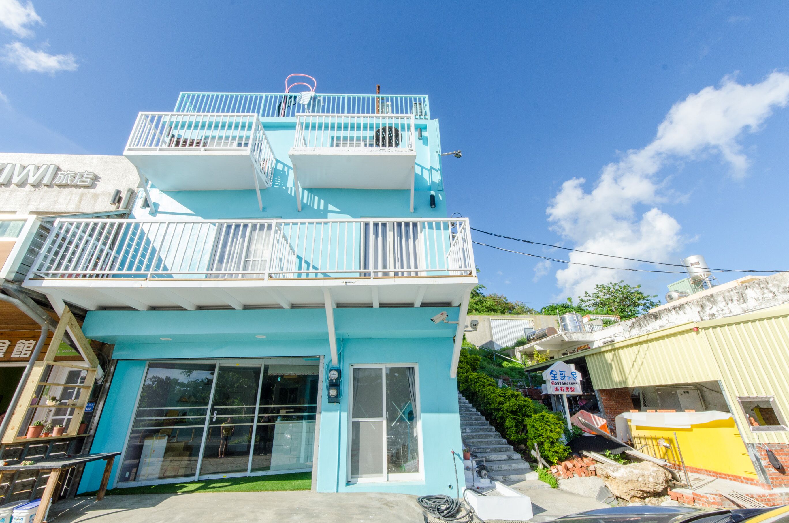A two-story building with a blue facade, a balcony on the upper floor, and a visible storefront on the ground floor.