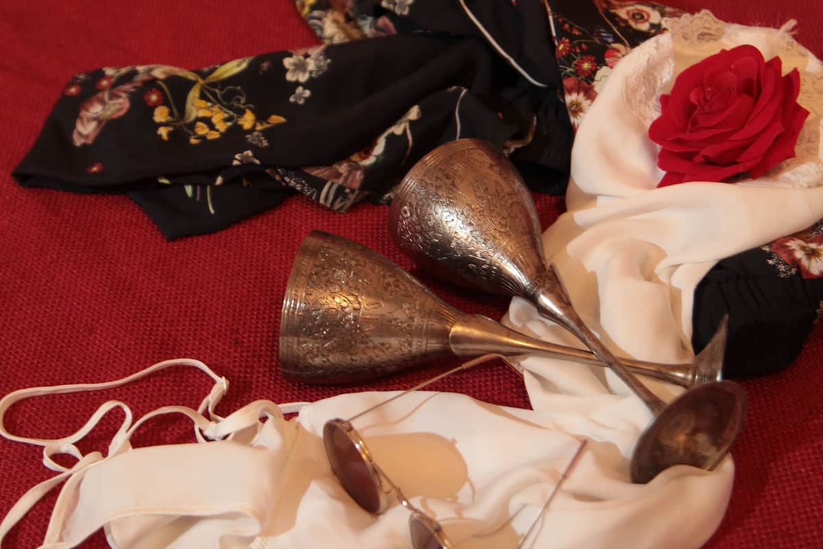 A collection of items including a black floral dress, a white dress, a red rose, and a pair of ballet shoes on a red fabric surface.