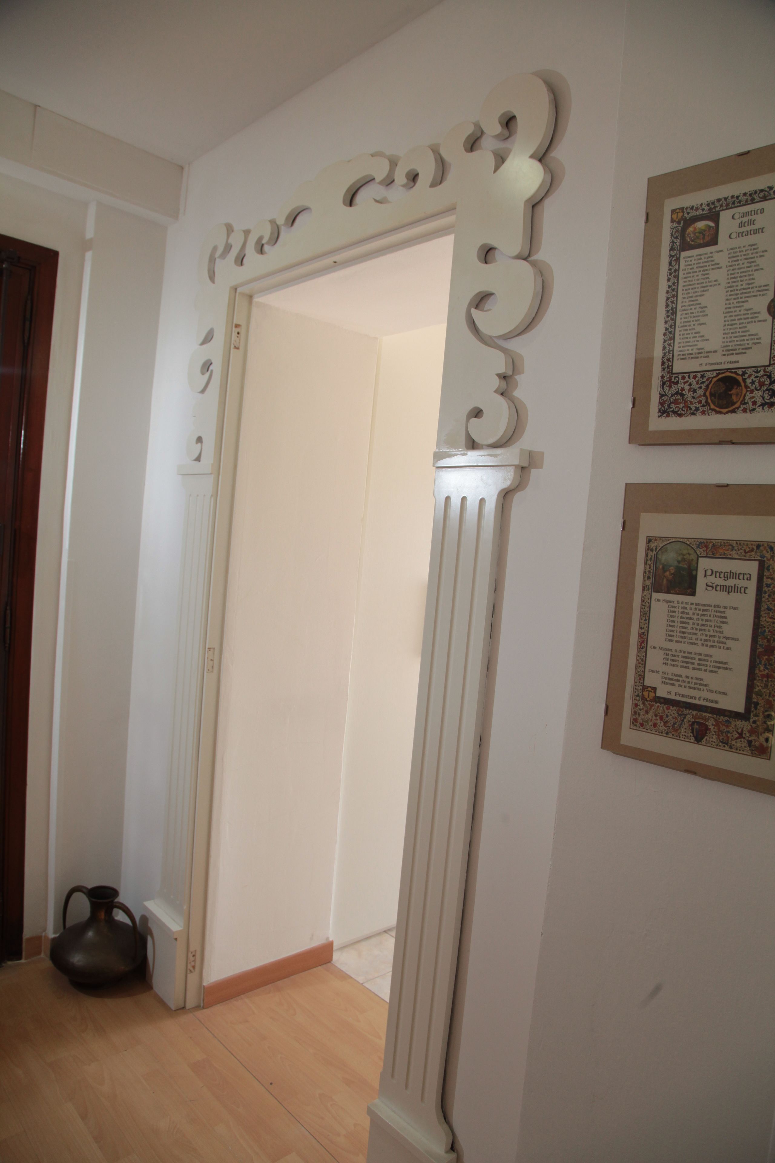 Um corredor com um pilar branco decorativo, uma placa informativa emoldurada e piso de madeira.