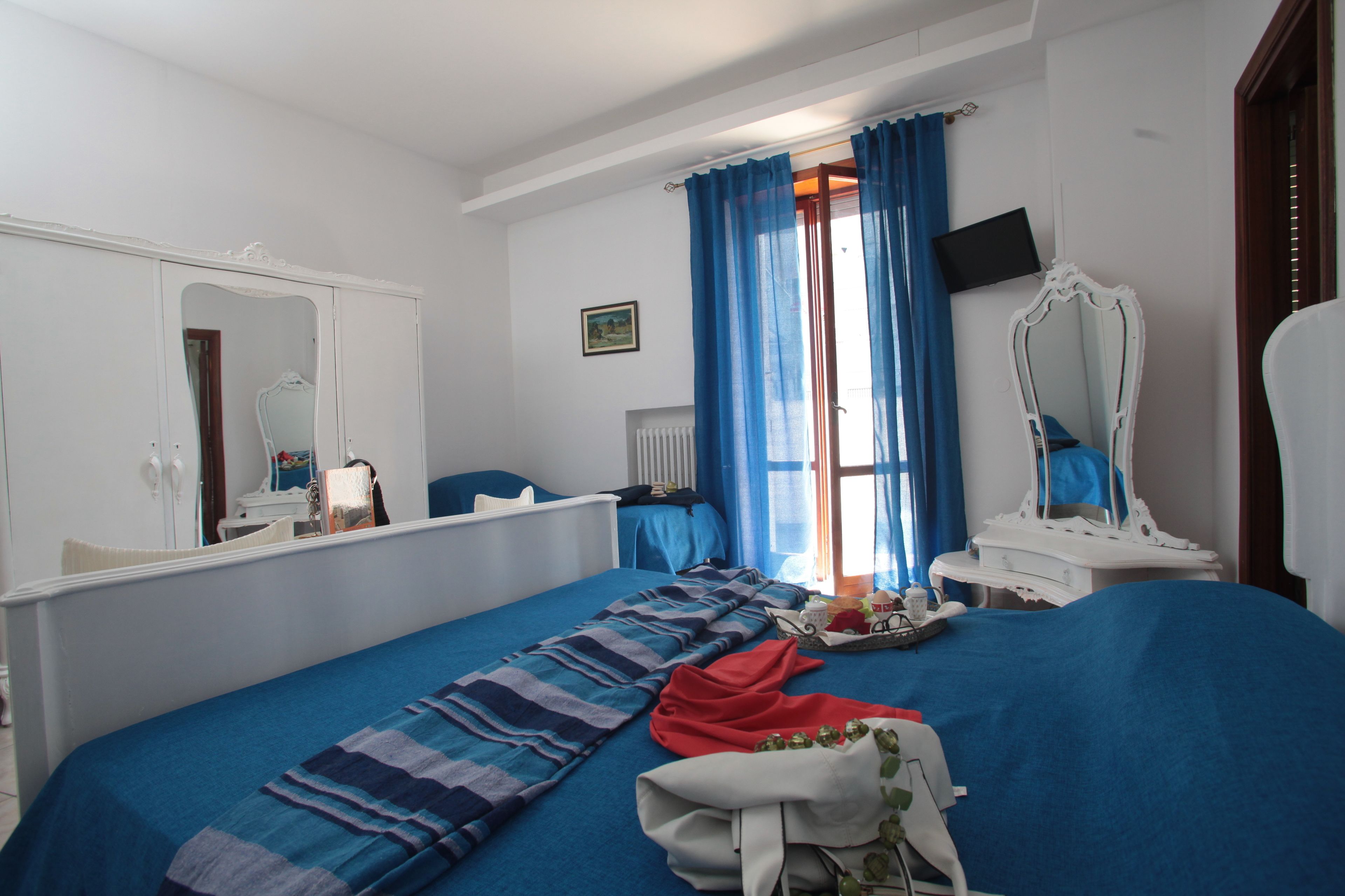 A bedroom with a large bed, a dresser, a mirror, a television, and a window with blue curtains.