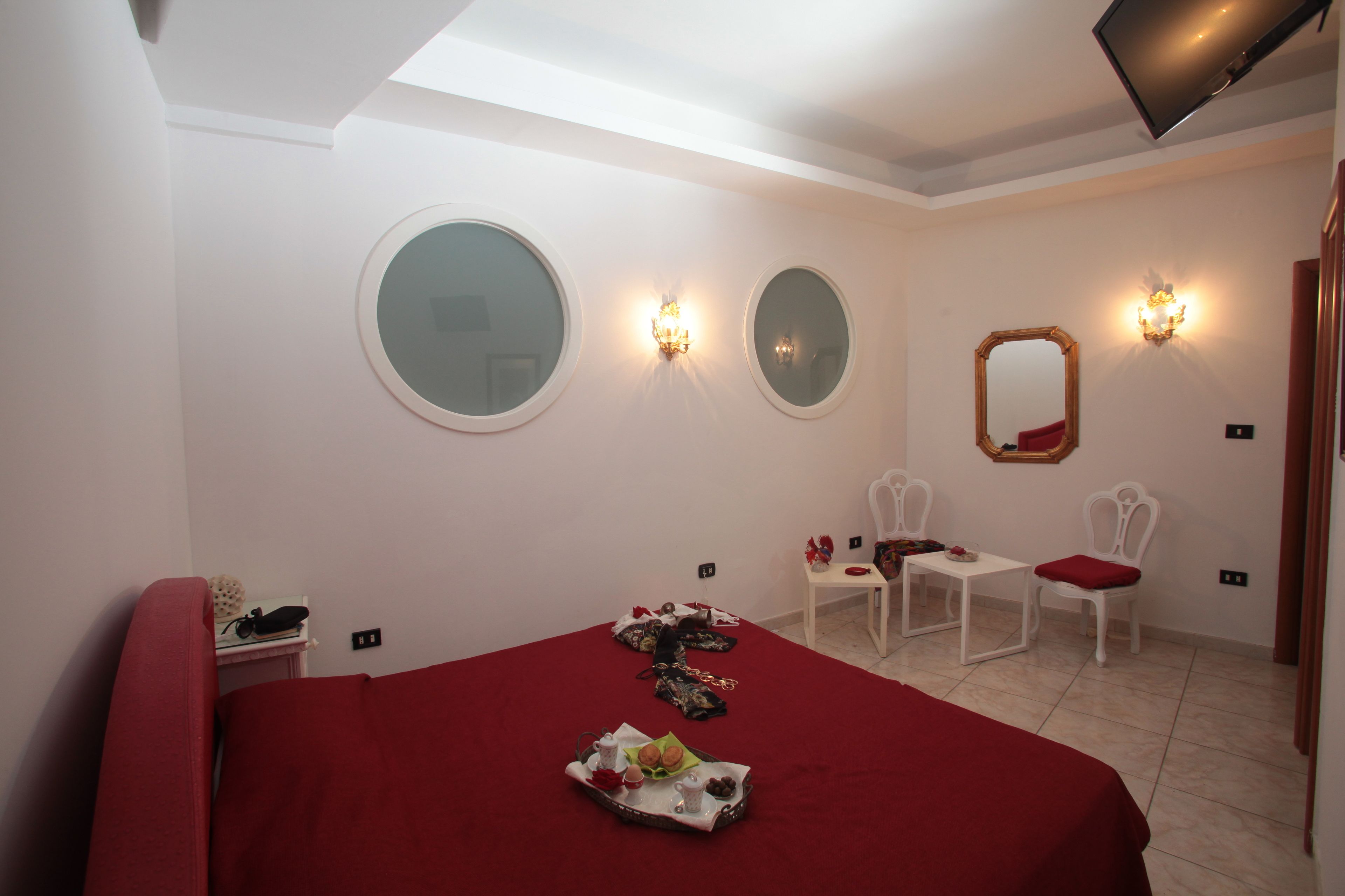 A hotel room with a large bed, two chairs, a small table, and a mirror on the wall.
