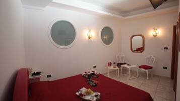 A hotel room with a large bed, two chairs, a small table, and a mirror on the wall.