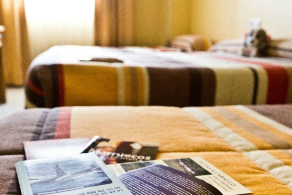 Una habitación de hotel con cama, mesita de noche y manta.