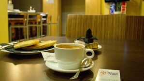 A dining table with a cup of coffee, a plate with a sandwich, and a spoon. There is a menu on the table. - Hotel María Luisa (Algeciras)