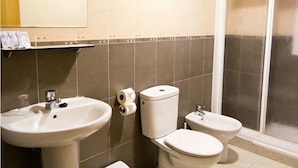 A bathroom with two toilets, a sink, and a shower area. - Hotel María Luisa (Algeciras)