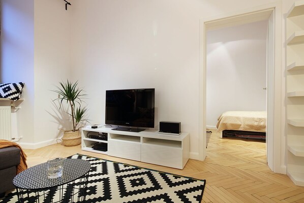 A modern living room with a flat-screen TV on a white entertainment unit, a patterned rug, and a grey sofa.