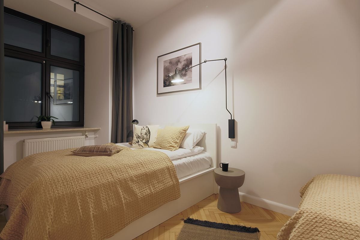 A bedroom with a bed, bedside table, lamp, window, and a framed picture on the wall.