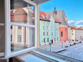 A view from a window of a building with a red roof, a green building with a clock tower, and a pink building.