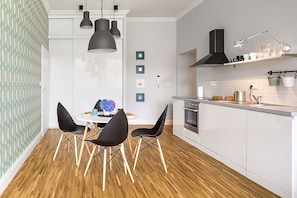 Una cocina moderna con armarios blancos, horno empotrado y extractor de aire negro. Hay un comedor con una mesa redonda y sillas negras.