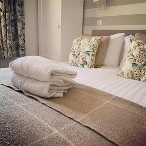A neatly made bed with floral pillows, a folded white towel, and a striped blanket. - Littletown Farm Guesthouse (Keswick)