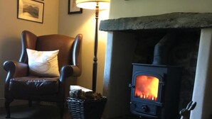 A cozy living room with a fireplace, a comfortable armchair, a table with a magazine, and a lamp. - Littletown Farm Guesthouse (Keswick)