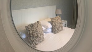 A bedroom with a round mirror, a bed with two pillows, a nightstand with a lamp, and a window with curtains. - Littletown Farm Guesthouse (Keswick)