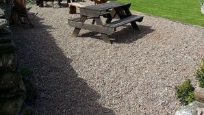 A gravel patio with picnic tables and chairs, a stone wall, and a view of rolling hills and mountains in the background. - Littletown Farm Guesthouse (Keswick)