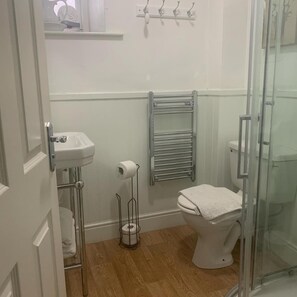 A bathroom with a toilet, a sink, a towel rack, and a glass shower enclosure. - Littletown Farm Guesthouse (Keswick)