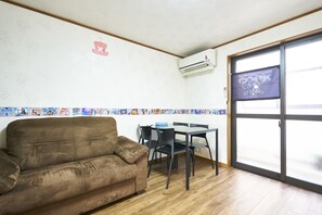 A room with a sofa, a table with chairs, a window with a view, and an air conditioning unit. - OTAKU (Kyoto)