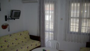 A room with a sofa, a small table with a plant, a TV, and a window with curtains. - Vural Apart Hotel (Cesme)