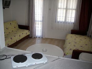 A small, well-lit room with two beds, a small table, and a white stove.