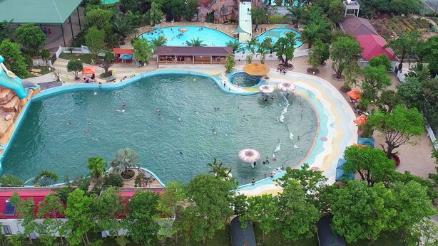 Una gran piscina al aire libre con varias pistas de natación, rodeada de palmeras y zonas de sombra.