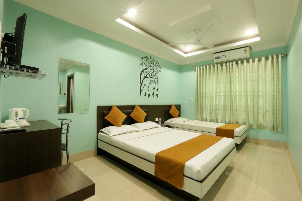 A hotel room with two beds, a desk with a coffee maker, a mirror, and an air conditioning unit.