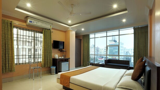 A hotel room with a bed, a desk, a chair, an air conditioner, and a view of the city. - Hotel Grand Luit (Guwahati)
