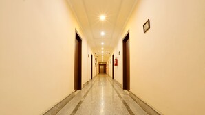 A long, well-lit hallway with a polished floor, doors on both sides, and a fire extinguisher on the right wall. - Hotel Grand Luit (Guwahati)
