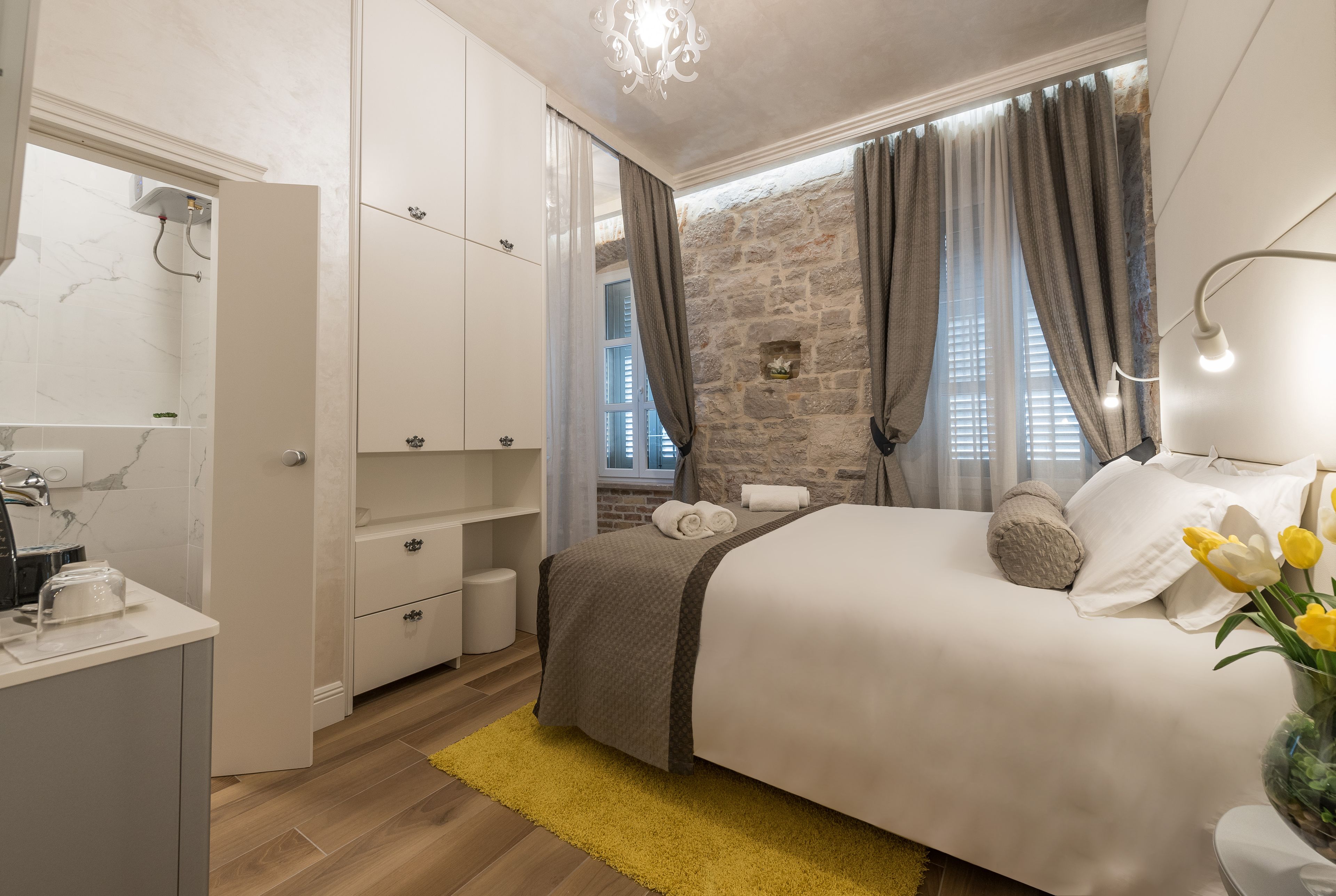 Una habitació amb llit, armari, bany i paret de pedra.