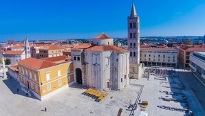 Una plaza histórica con una iglesia destacada y un alto campanario, rodeada de edificios tradicionales con tejados de tejas rojas.