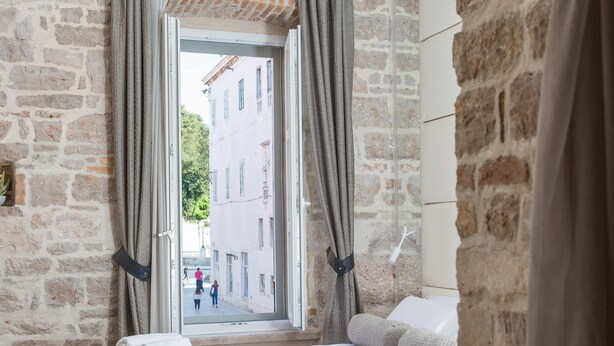 Un dormitorio con una cama, una mesita de noche con una taza y vistas a una calle a través de una ventana.