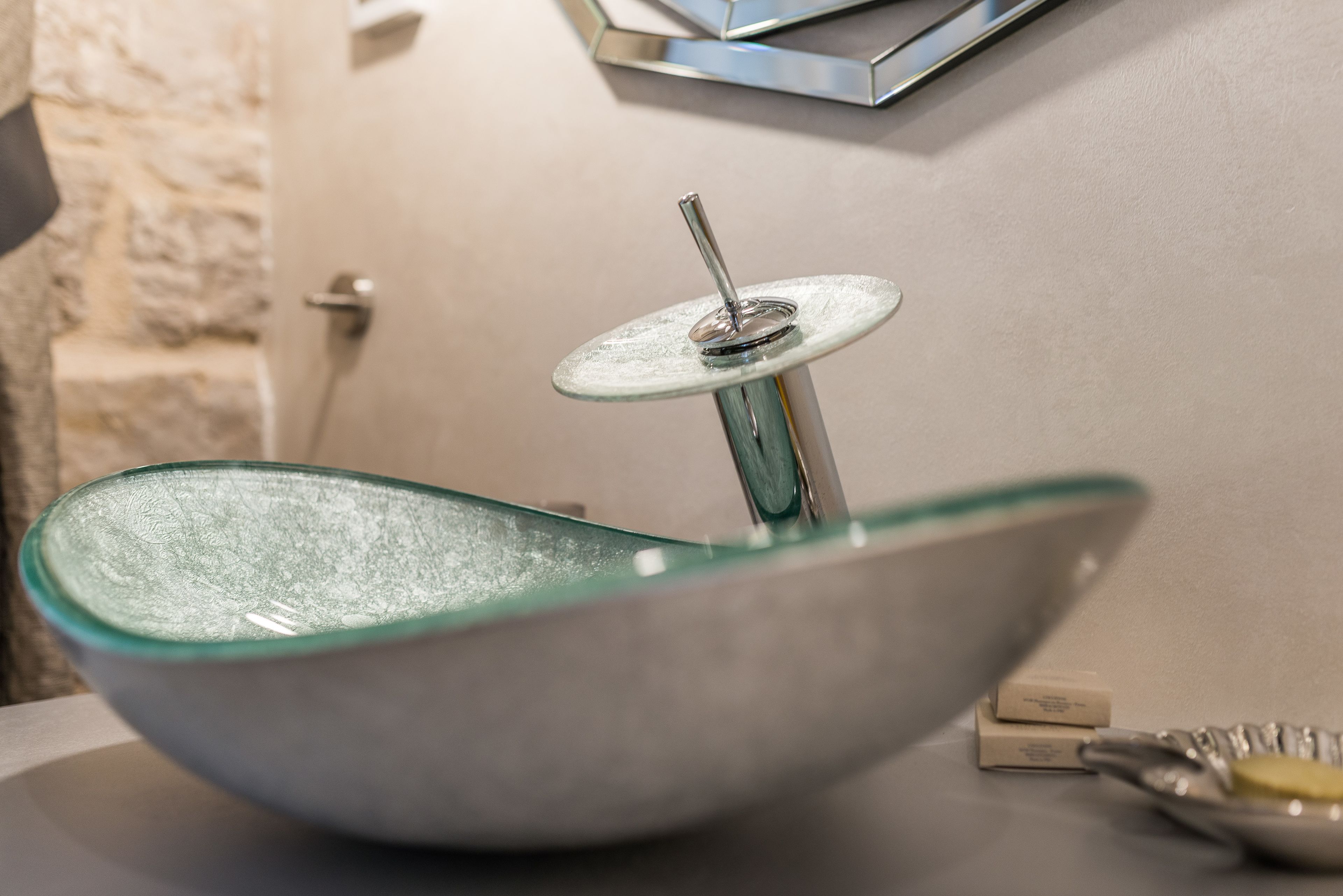 A modern bathroom with a glass basin and a wall-mounted soap dispenser.