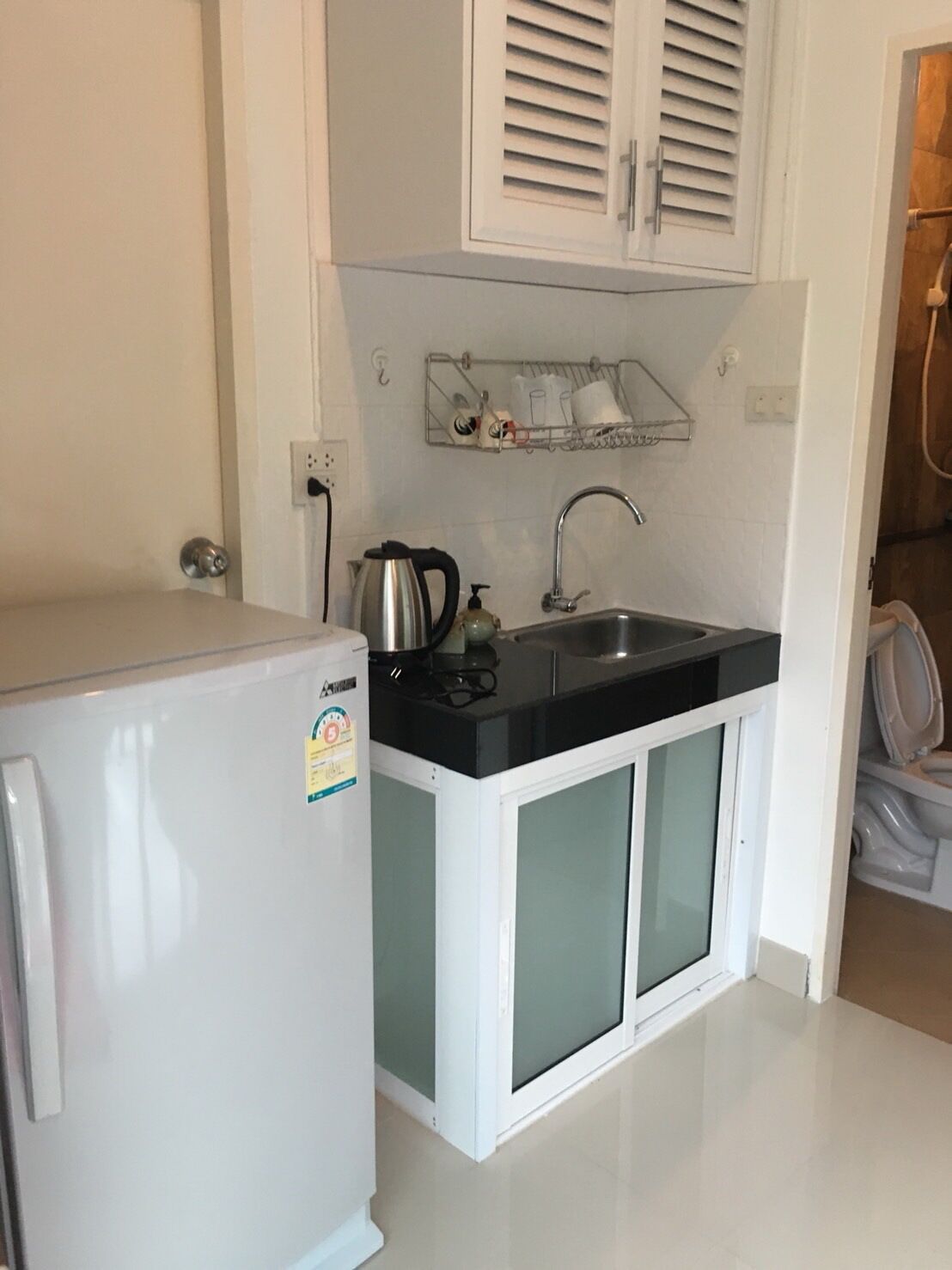 A compact kitchen with a refrigerator, a sink, and a kettle.