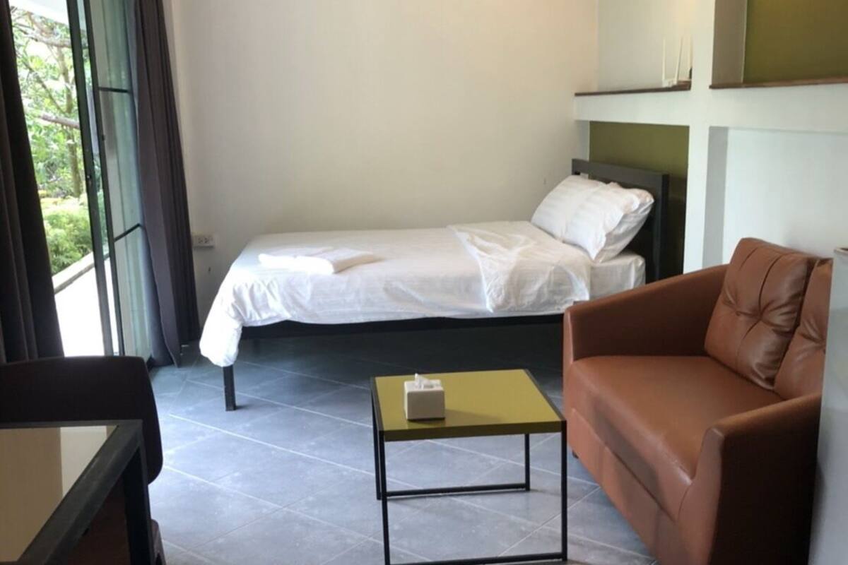 A room with a bed, a brown leather sofa, a small table, and a chair.
