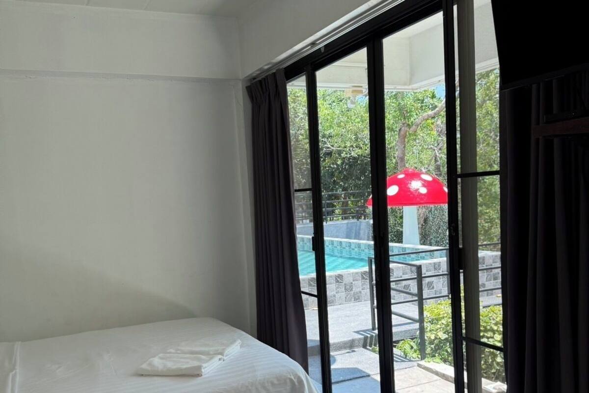 A hotel room with two beds, a large window with curtains, and a view of an outdoor pool area.