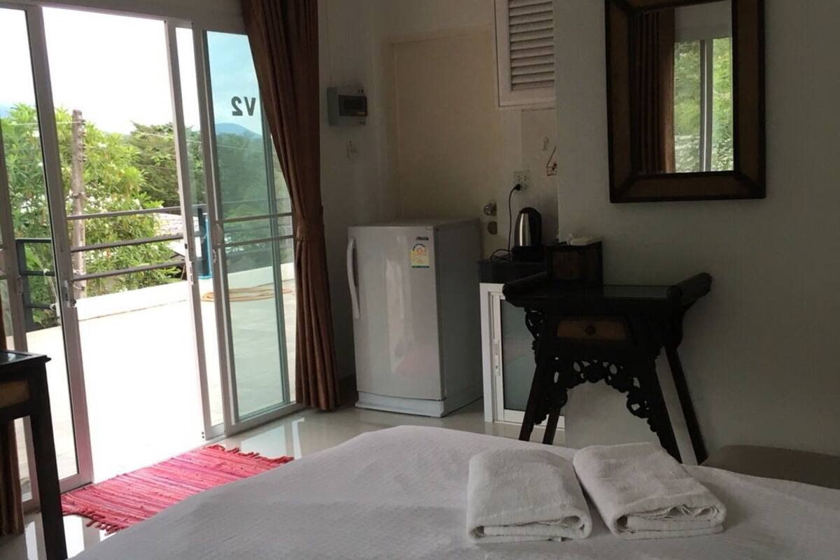 A hotel room with a bed, a desk, a refrigerator, and a sliding glass door to the outside.