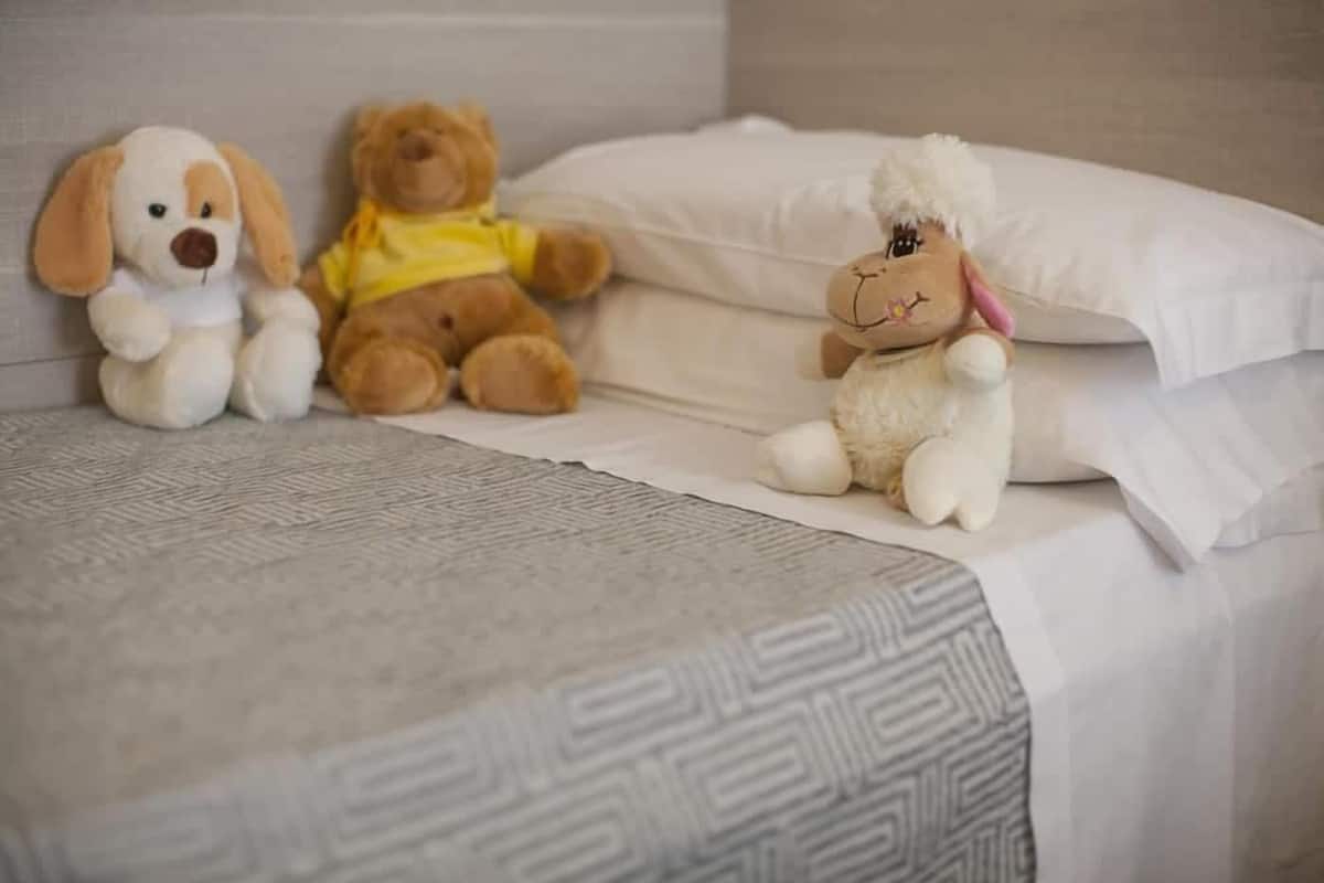 A bed with a patterned bedspread, two stuffed animals, and a white pillow.
