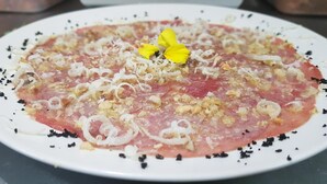 Lautasella on raakaa kalaa, jonka päällä on sipulia, yrttejä ja keltainen kukka.