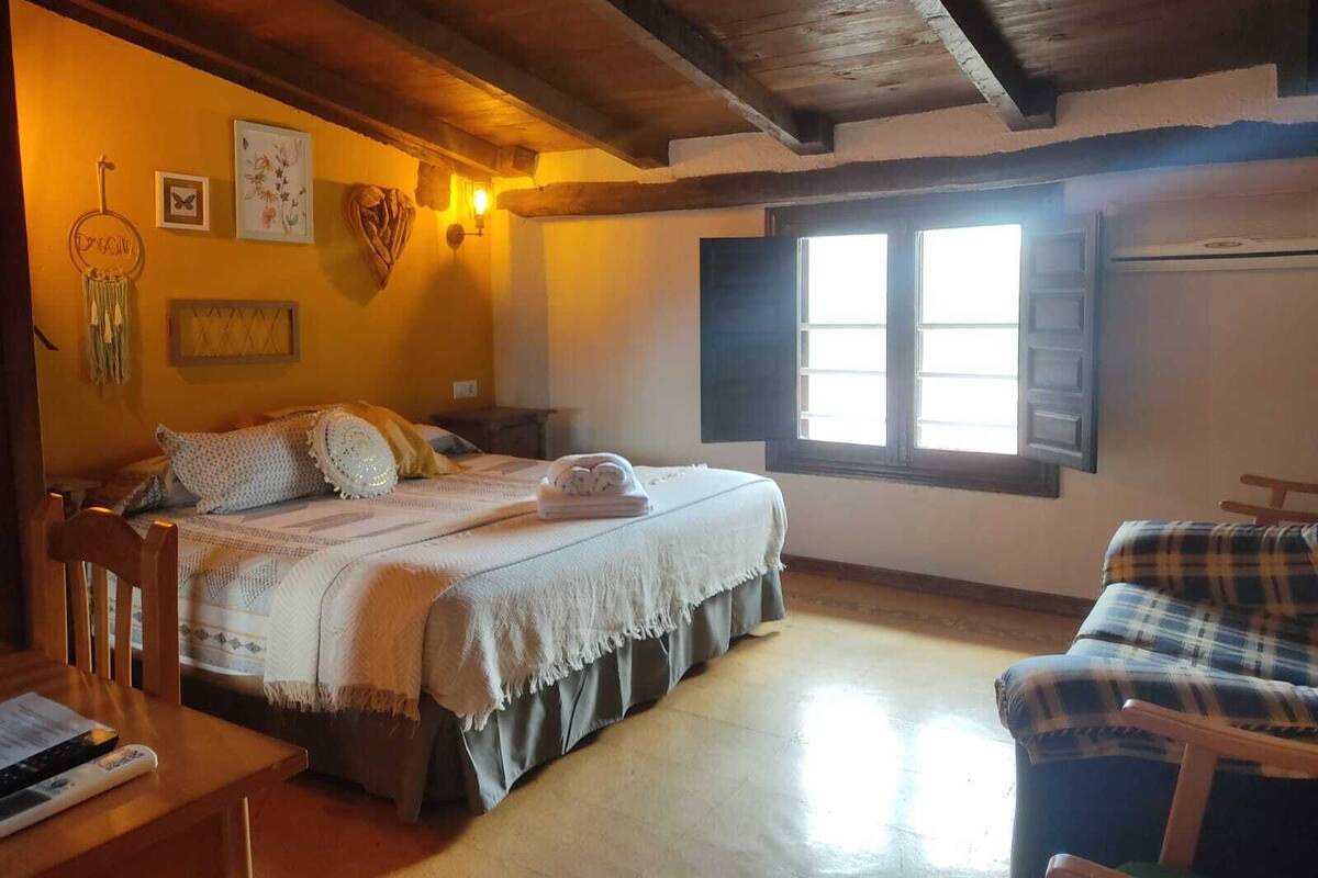Um quarto aconchegante com uma cama, uma cadeira, uma mesa e uma janela.