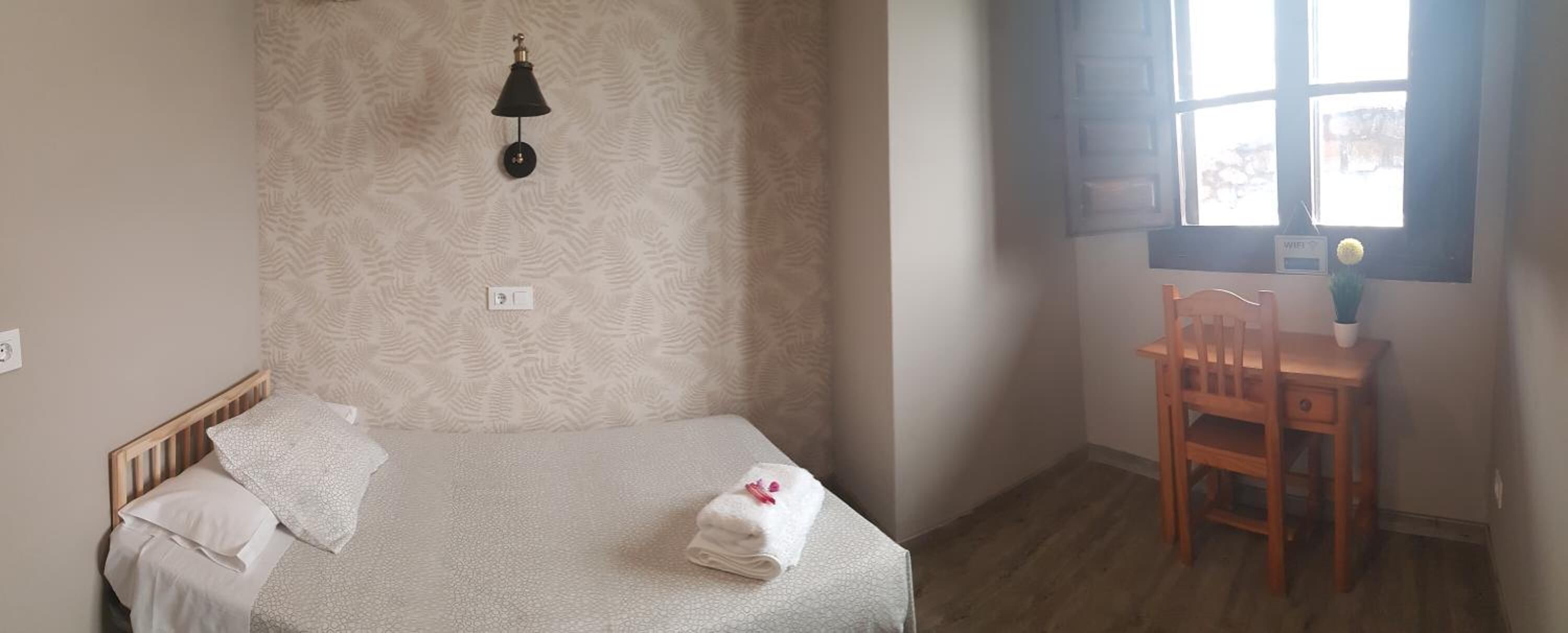 Un dormitorio con cama, escritorio y ventana.