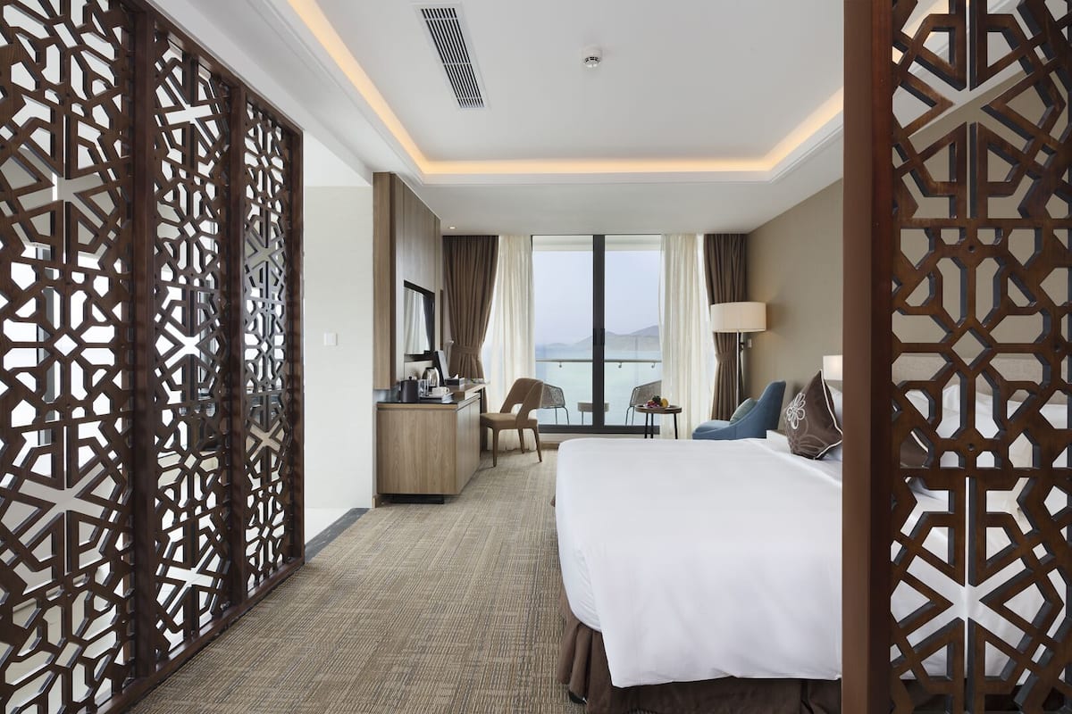 A hotel room with a large bed, a desk, a chair, and a view of the sea.