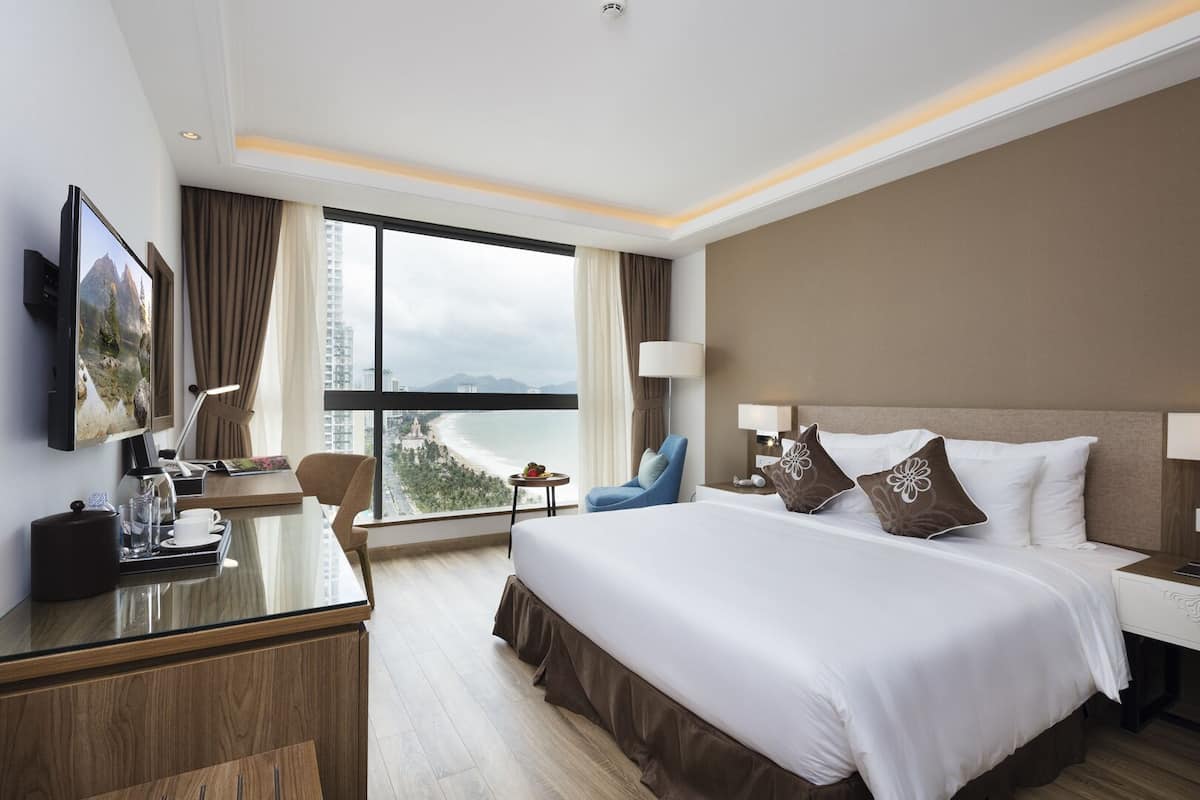 A hotel room with a large bed, a desk with a coffee maker, a chair, and a TV on the wall.