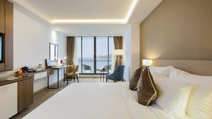 A hotel room with a large bed, a desk, a chair, and a view of the sea. - Comodo Nha Trang Hotel (Nha Trang)