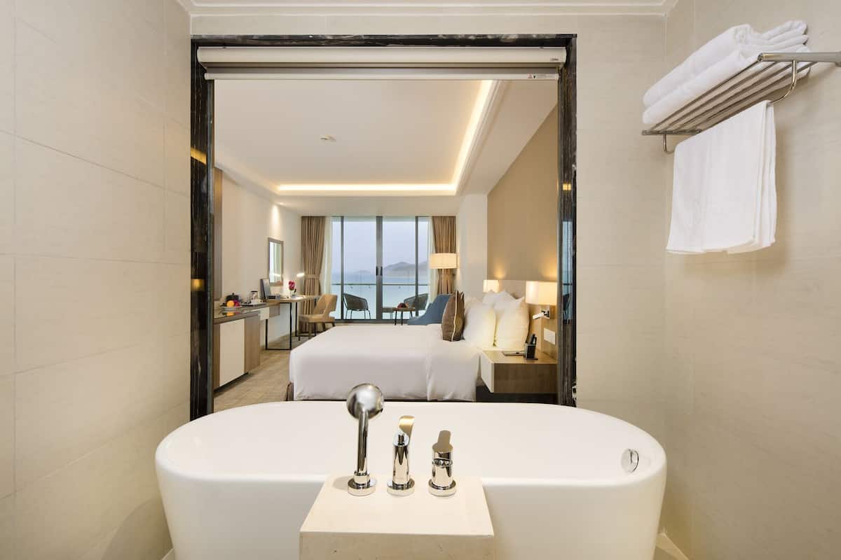 A modern hotel bathroom with a large bathtub, a mirror, and a view of the room.