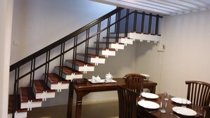 A dining area with a wooden table set for four, a staircase with black railings, and a ceiling light fixture. - Colombo Residence - Luxury House - B & B (Colombo)