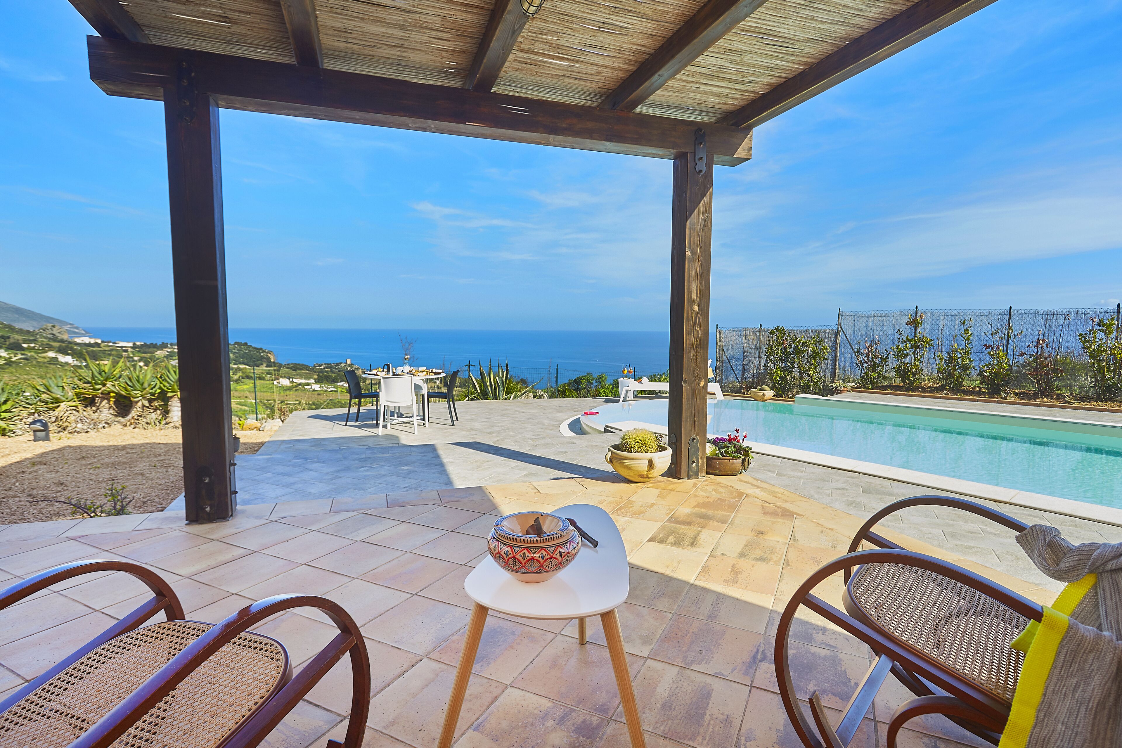 Um alpendre coberto com vista para o oceano, uma piscina e mobiliário de exterior.